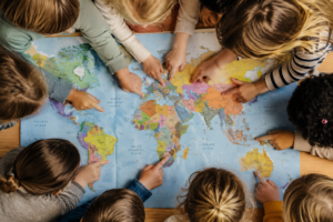 Kinder zeigen gemeinsam auf verschiedene Länder einer Weltkarte und entdecken spielerisch die Welt.